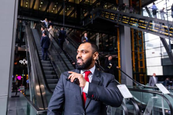 Mitie male security guard in a suit standing at the bottom of escalators